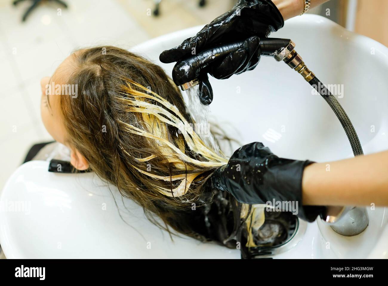 The girl is washed her hair in the salon. You can see the hands of the master. A few streaked strands. Preparing for hair coloring. Stock Photo