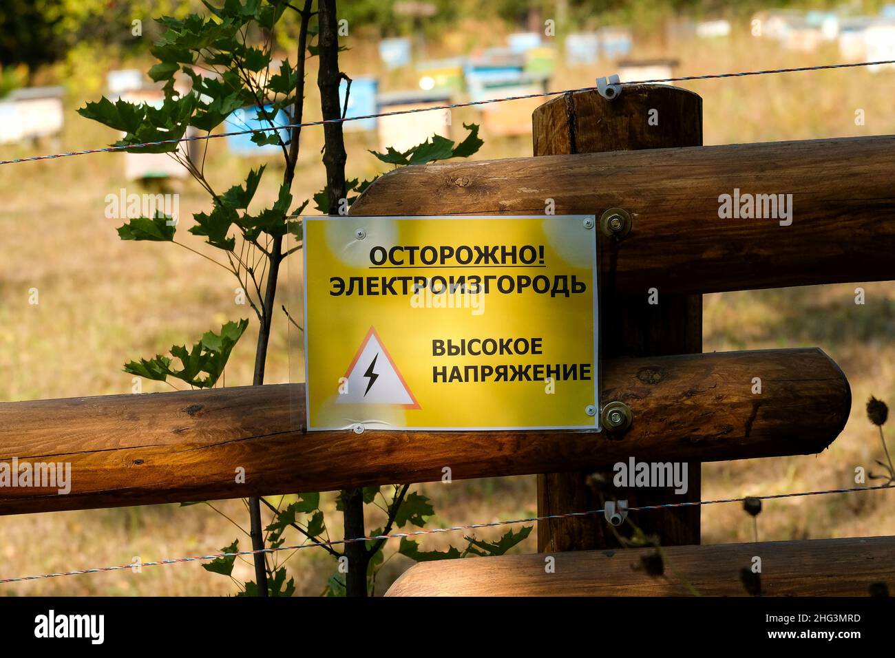 Warning on a wooden fence. Russian text: Caution. The fence is energized. High voltage. Stock Photo