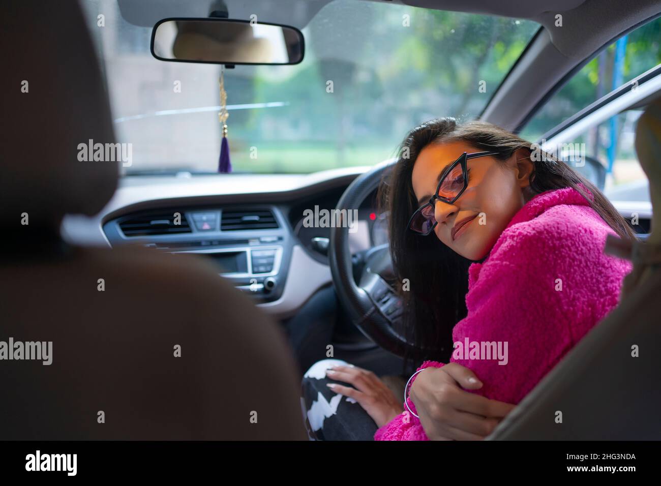 A young woman sitting in the driving seat of car looking at back seat. Stock Photo