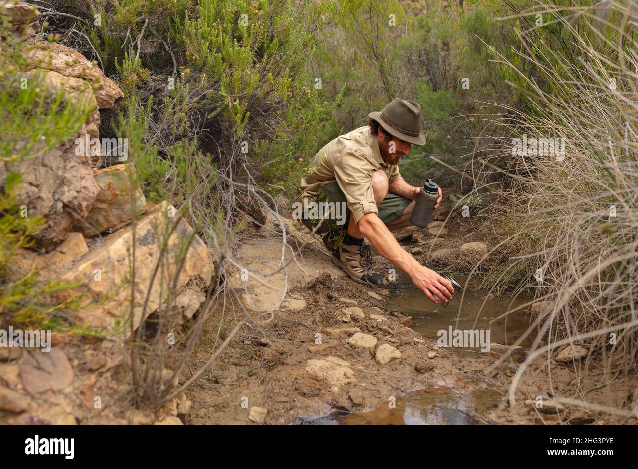 Young caucasian male adventurer collecting water from small pond amidst