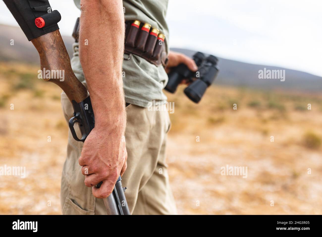Midsection of young man hunter holding rifle and binoculars in forest Stock Photo