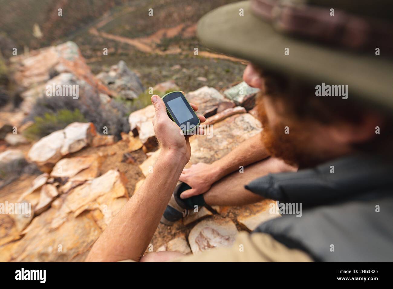 Young male caucasian adventurer using smartphone while sitting on mountain top Stock Photo