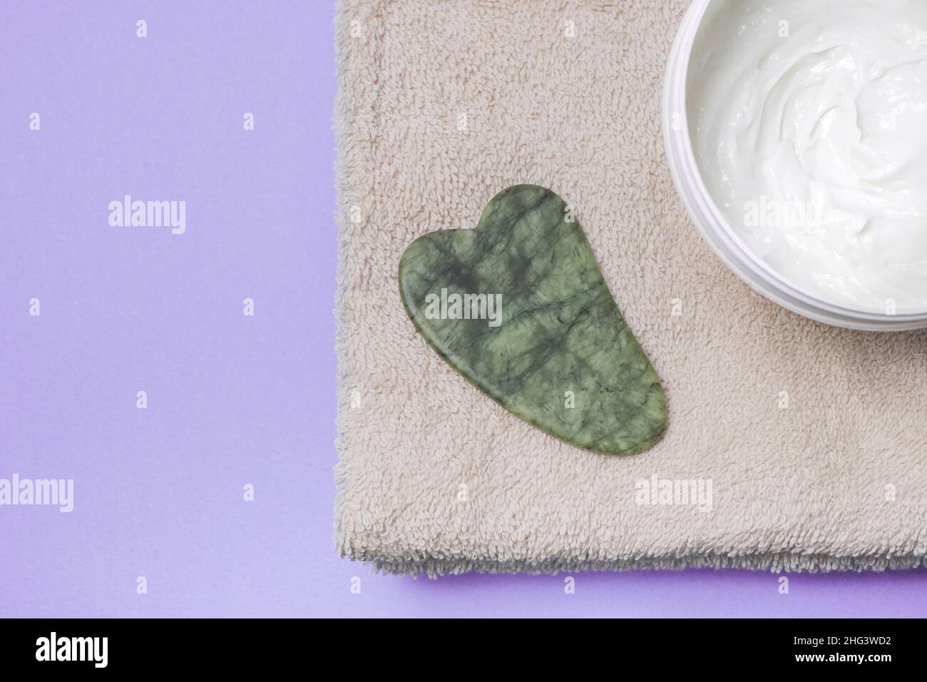 Face care and massage. Face gua sha stone with cream and on a towel on