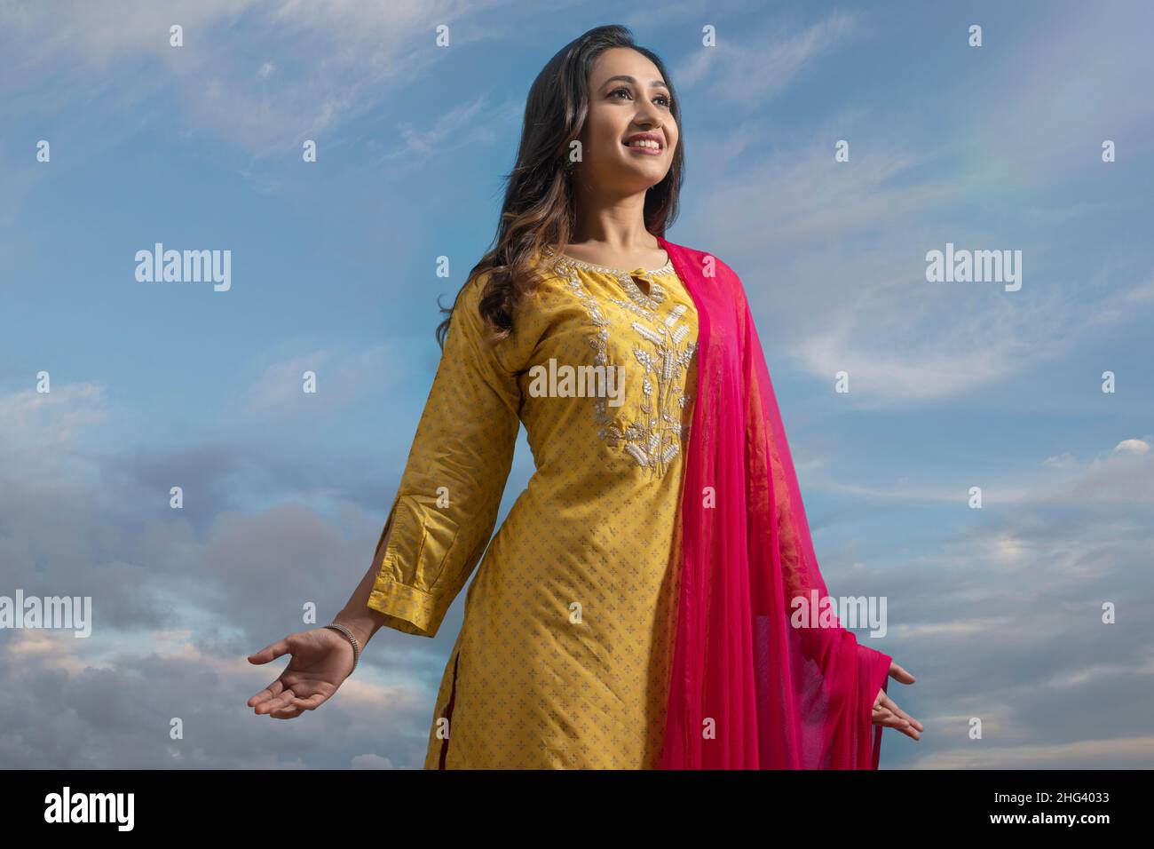 Happy woman in yellow salwar standing under the blue sky with her arms outstretched Stock Photo