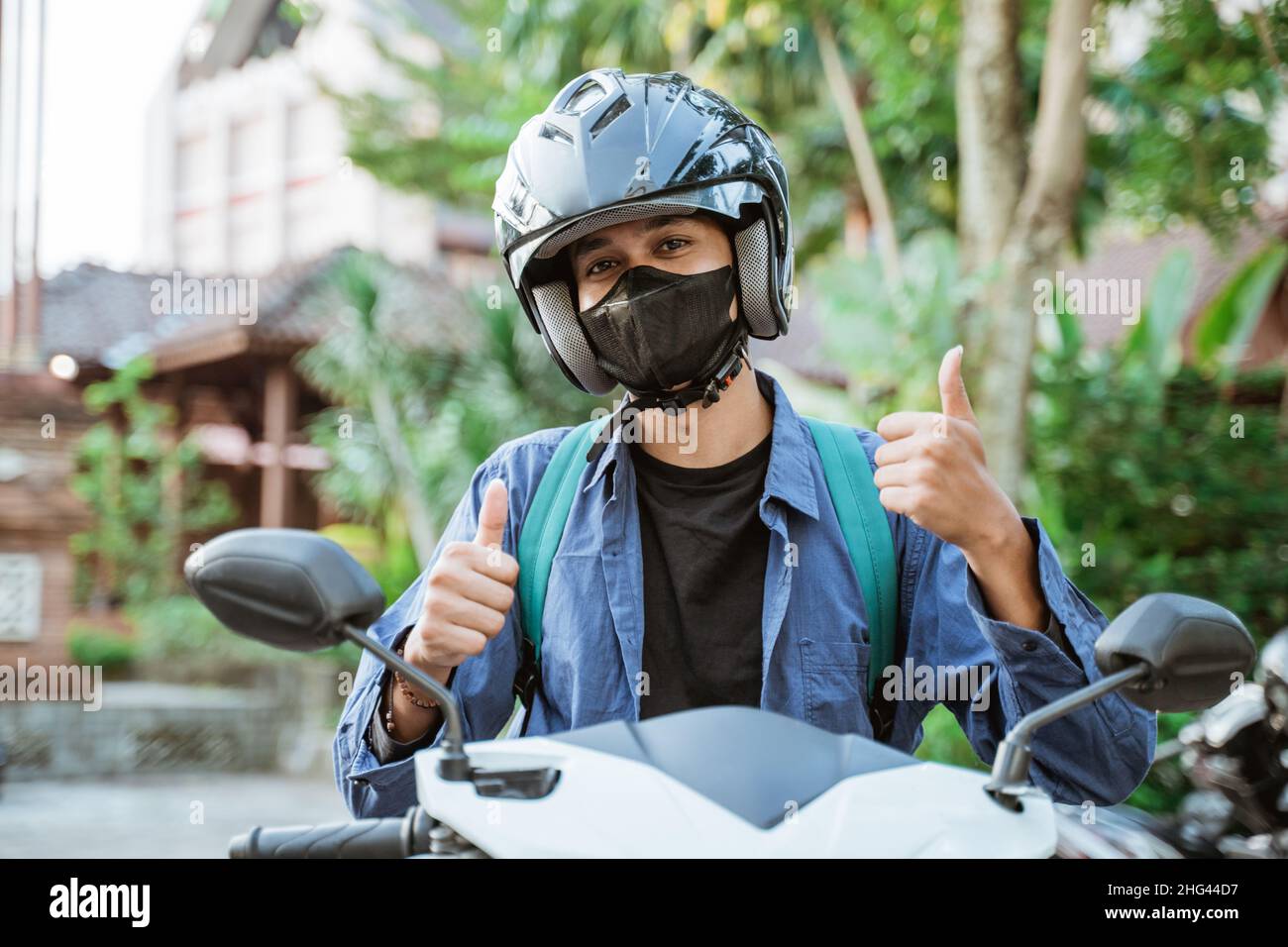 Man wearing helmet and mask with thumbs up on motorcycle Stock Photo