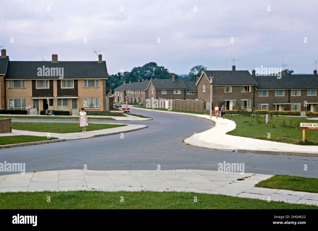 A view west along Rother Crescent in the Gossops Green area of Crawley ‘New Town’, West Sussex, England, UK in 1966. The neighbourhood, west of the town centre, was one of 14 suburbs developed to create the post-war ‘new town’. After the World War II, in order to relocate those in London’s poor or bombed-out housing, large numbers of people and jobs were moved to new towns around SE England and Crawley was the one of these – a vintage 1960s photograph. Stock Photo