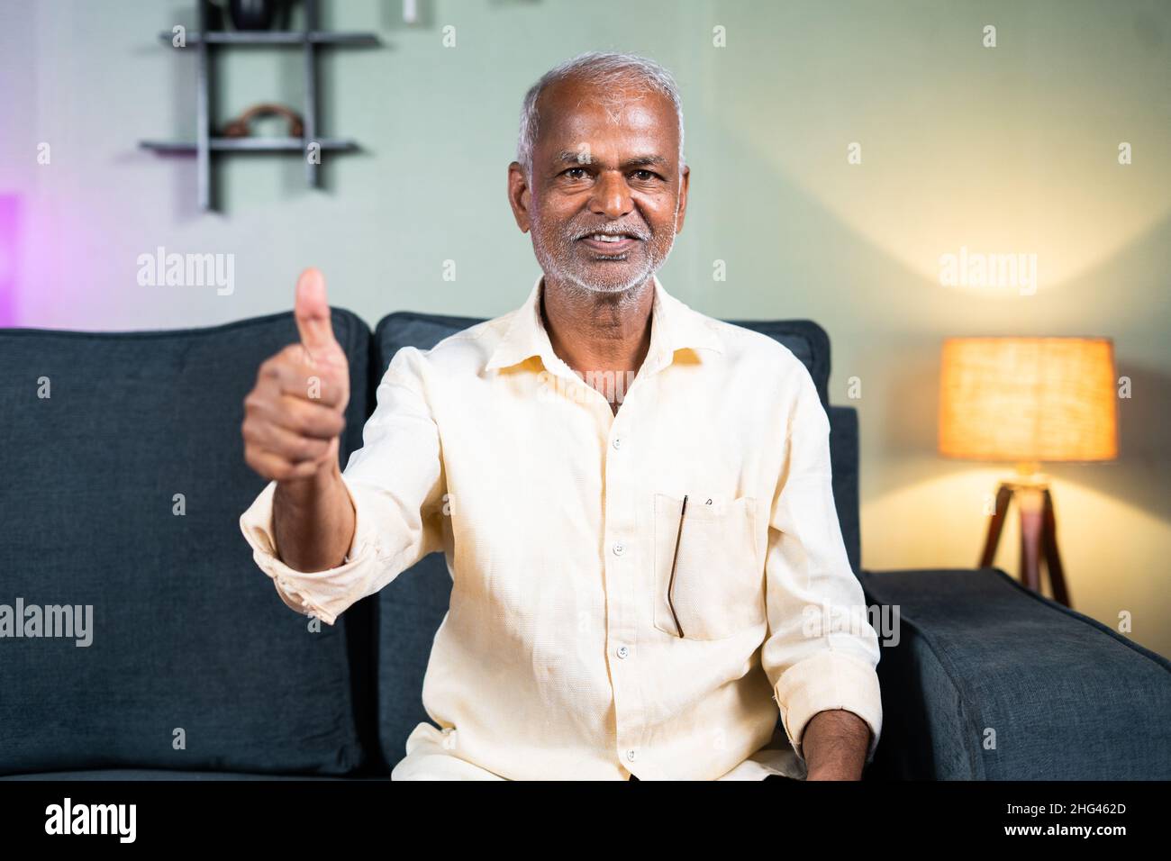 Indian senior old man showing thumbs up sign or hand gesture by looking at camera at home - cocnept of happiness or satisfaction about Healthcare and Stock Photo