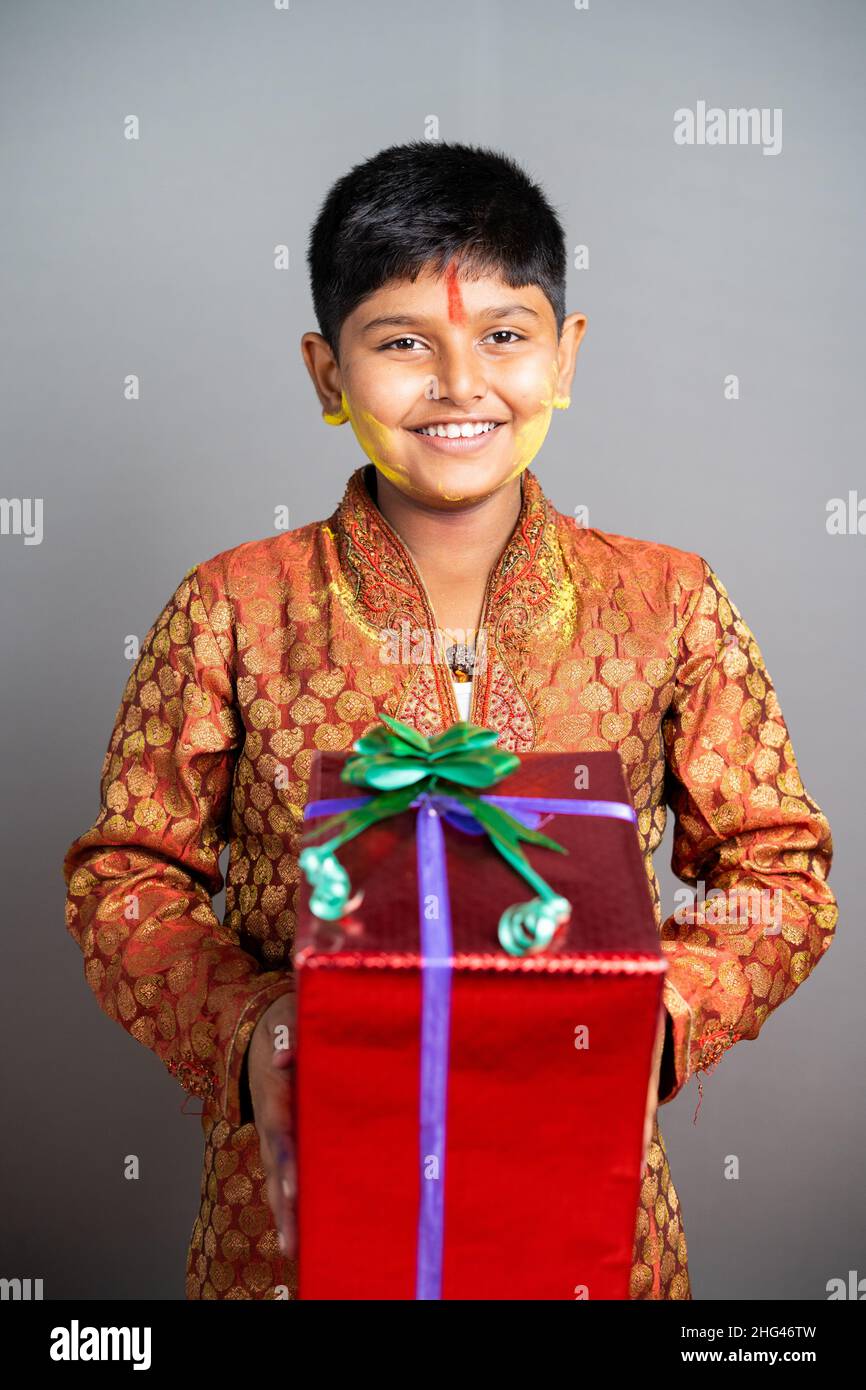 Happy Young kid with holi colors applied on face holding gift box by looking at camera - concept of hoi festival celebrations and gift promotion Stock Photo