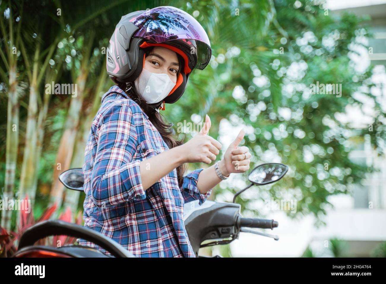 woman wearing helmet and mask with thumbs up on motorbike Stock Photo