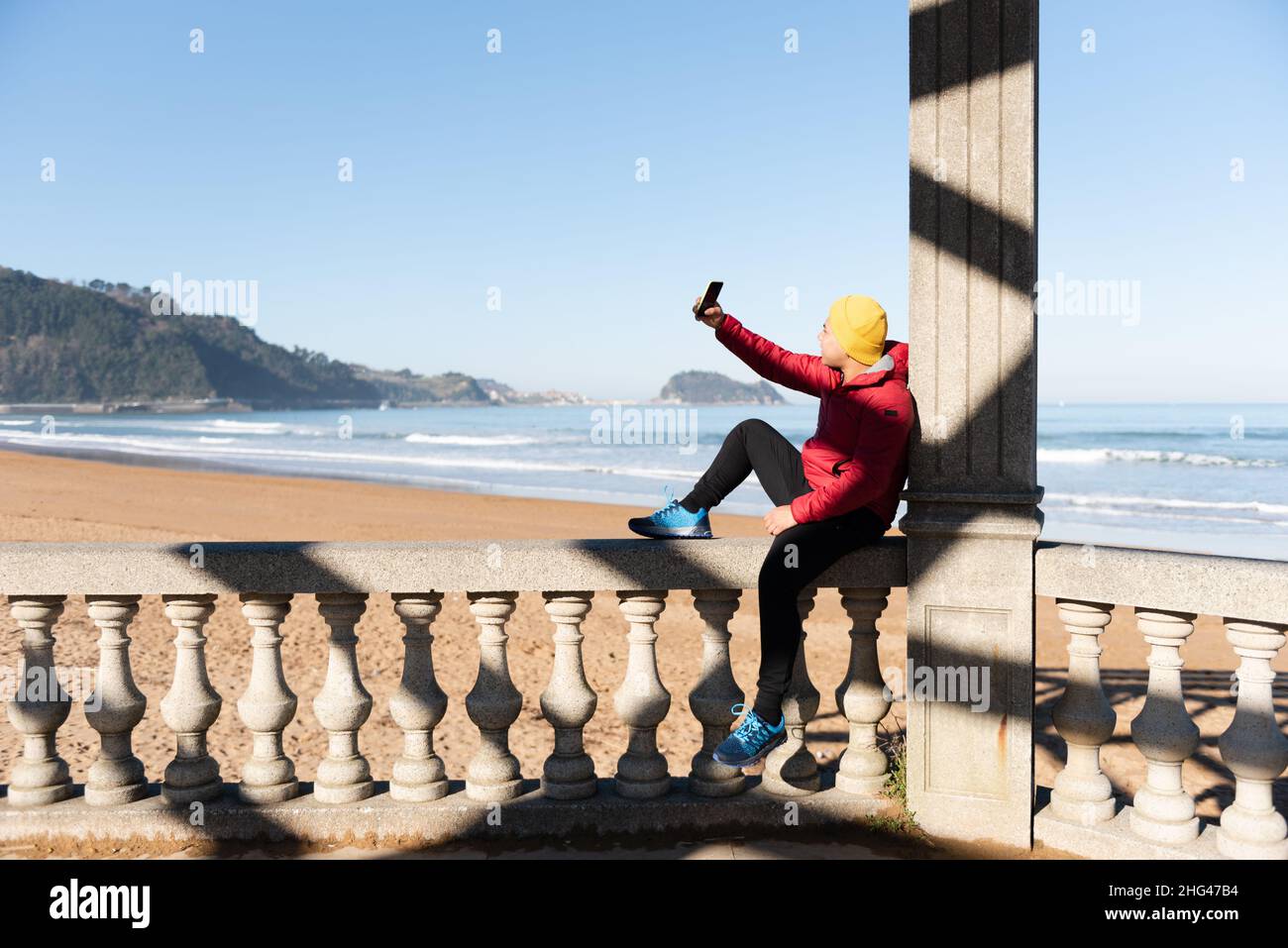 Latin teenager taking a selfie sitting at seaside. Stock Photo