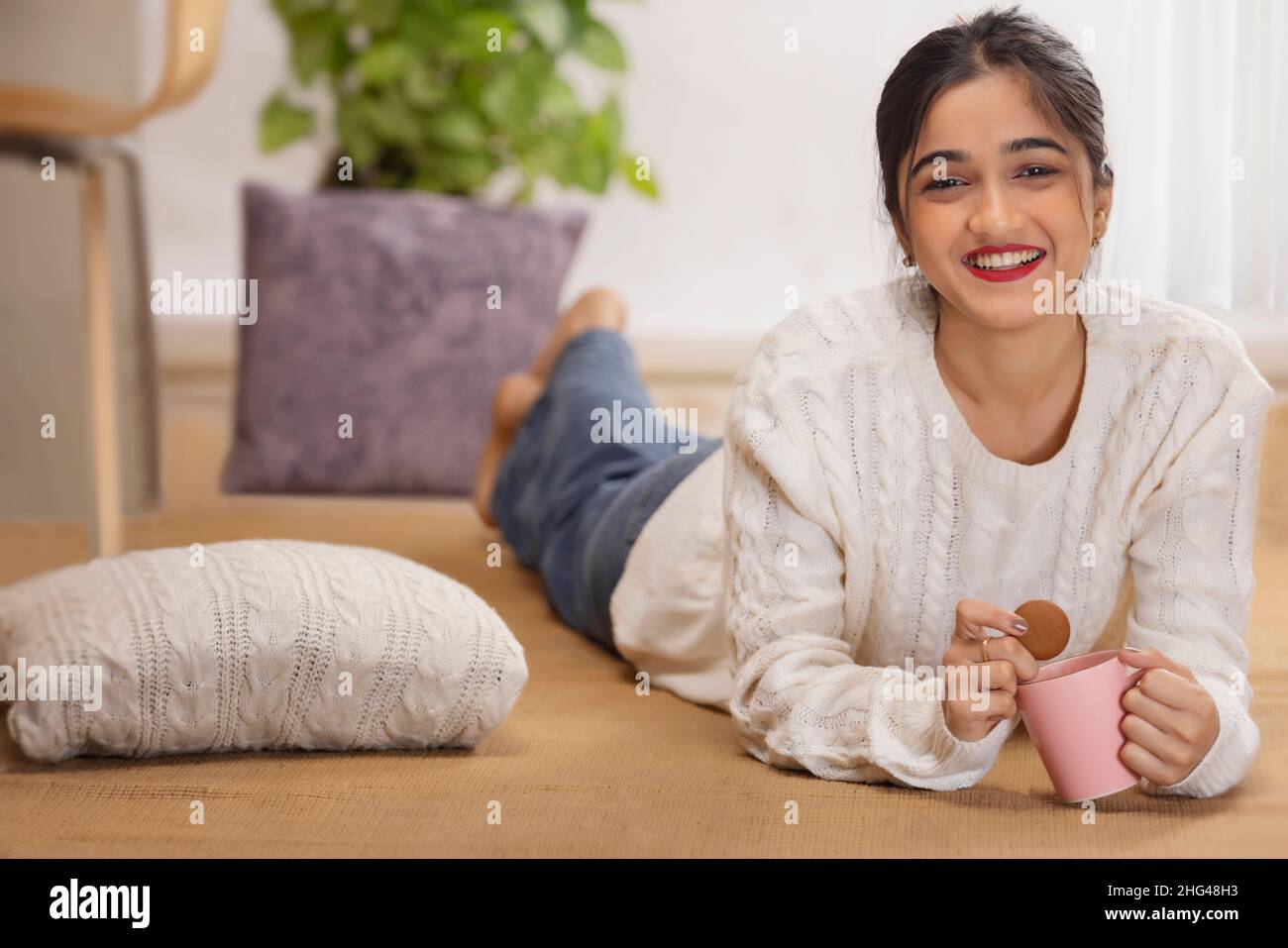 Happy girl with a cup of tea and cookie lying down on floor Stock Photo ...