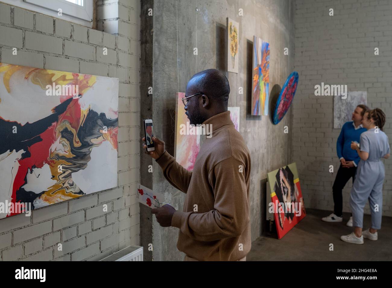 Young African male visitor of art gallery taking photo of painting on