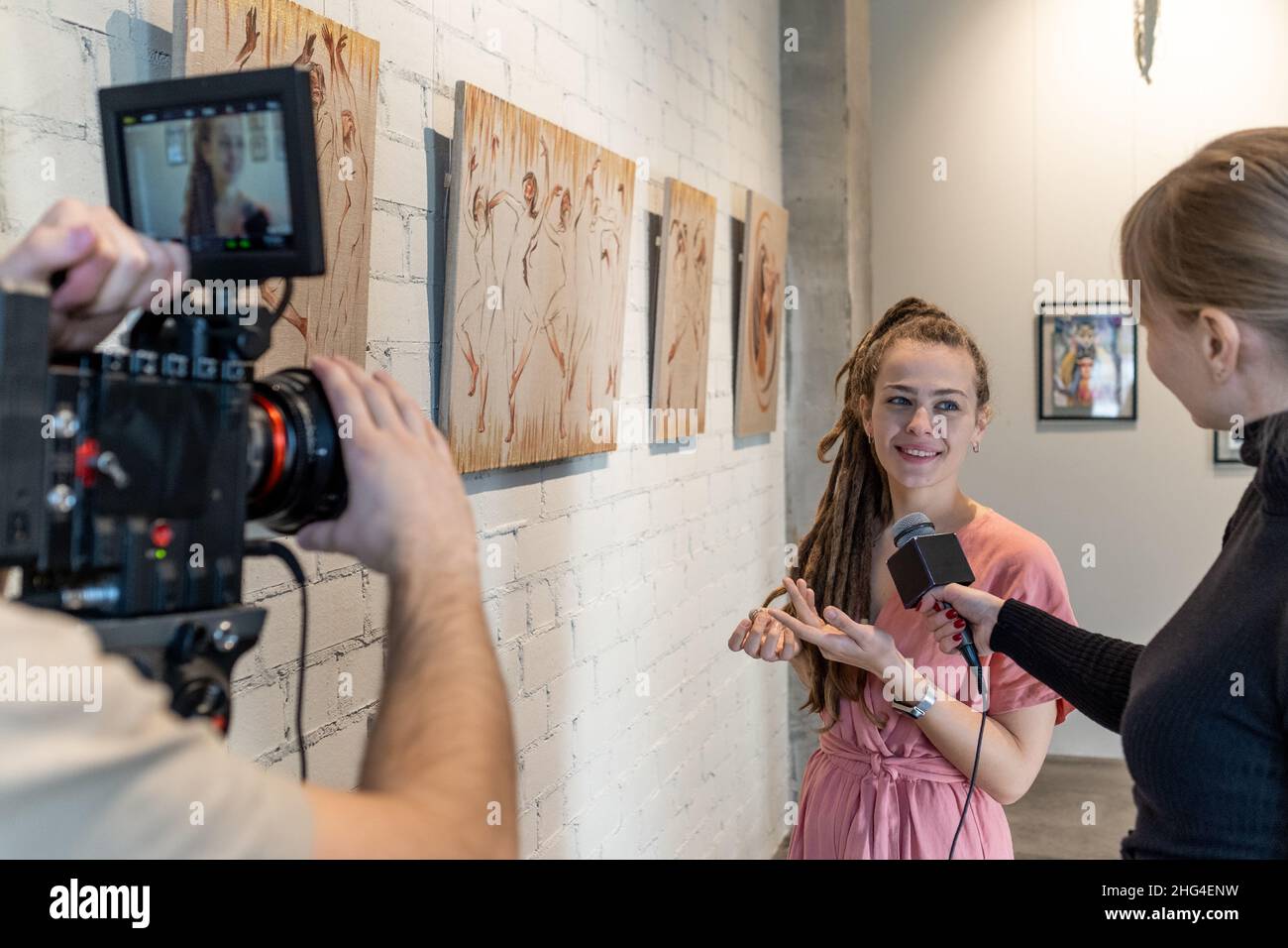 Happy young female guide of art gallery giving interview to journalists during presentation of new artwork collection Stock Photo