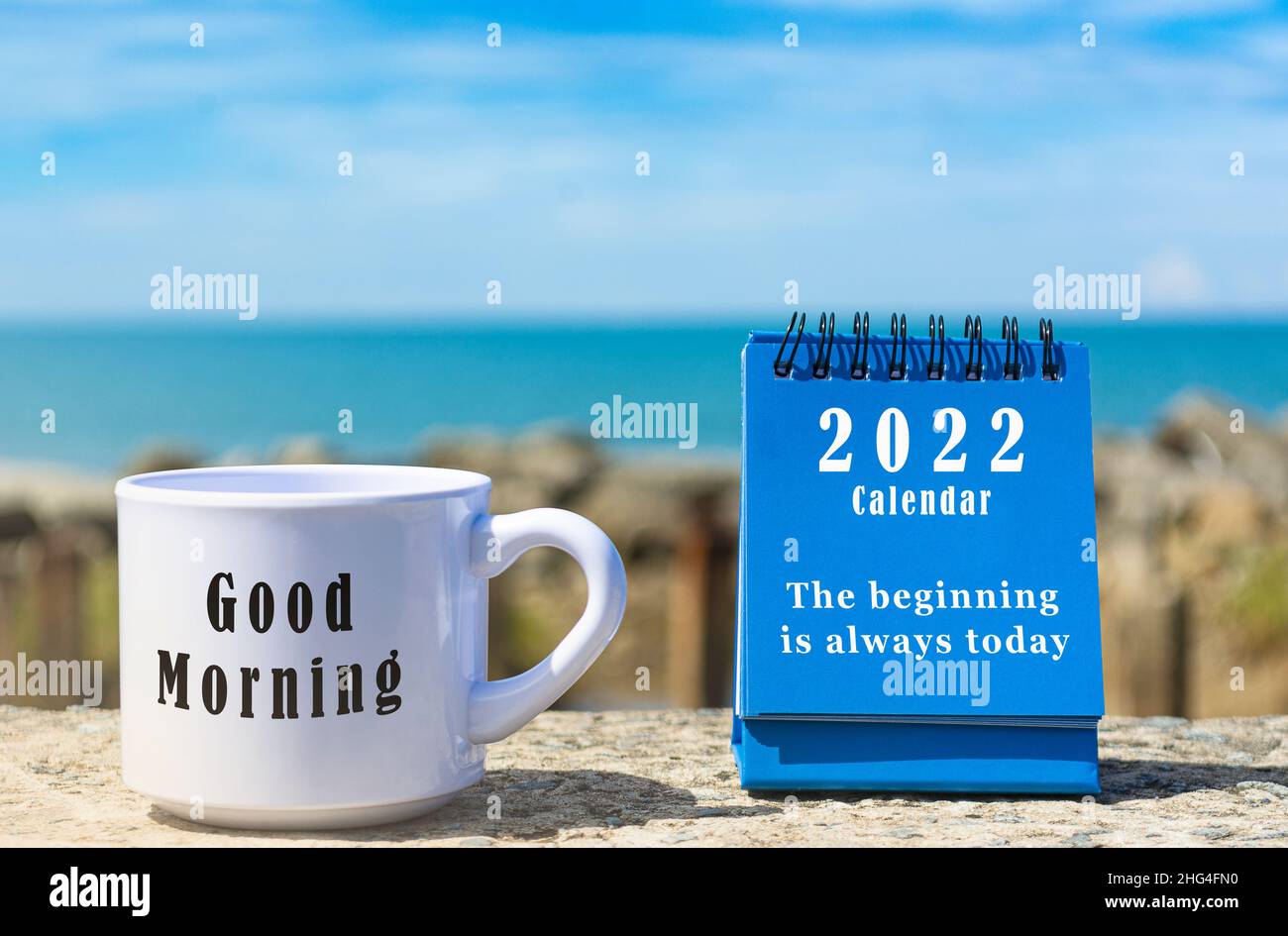 Motivational and Inspirational quote on blue standing notepad. Text on white coffee cup on blurred beach background and blue sky and clouds Stock Photo