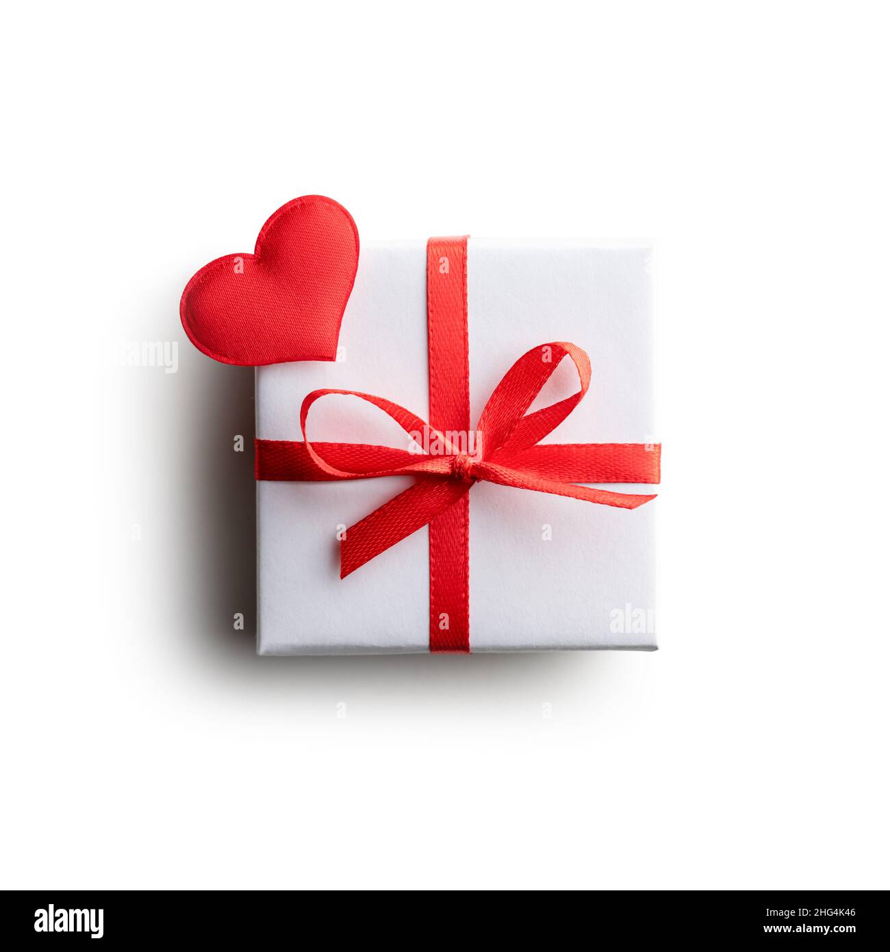 Gift box with red ribbon bow and red textile heart isolated on white background. Valentines day and love concept Stock Photo