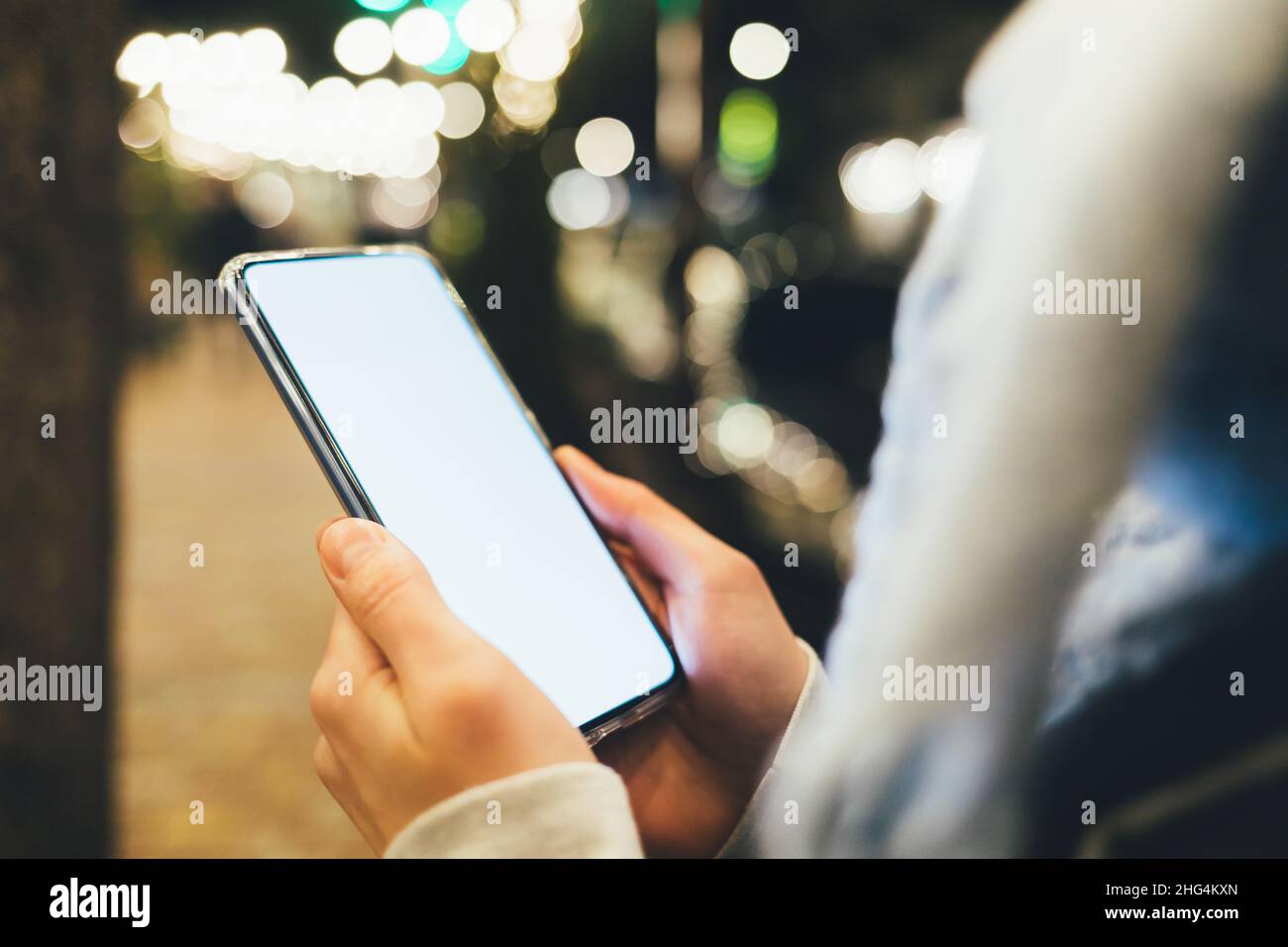Female hands holding modern smartphone with blank screen on illuminated ...