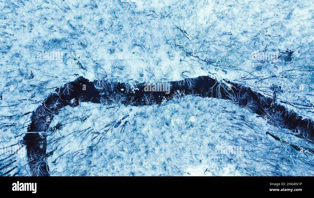 Top down view of small river in snow covered winter forest, drone view Stock Photo