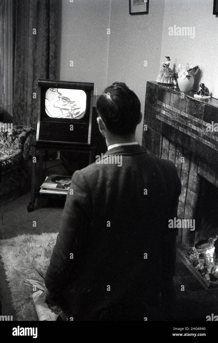 1950s, historical, in a living room, standing by an open fire, a man looking at a small television set of the era, England, UK. Stock Photo
