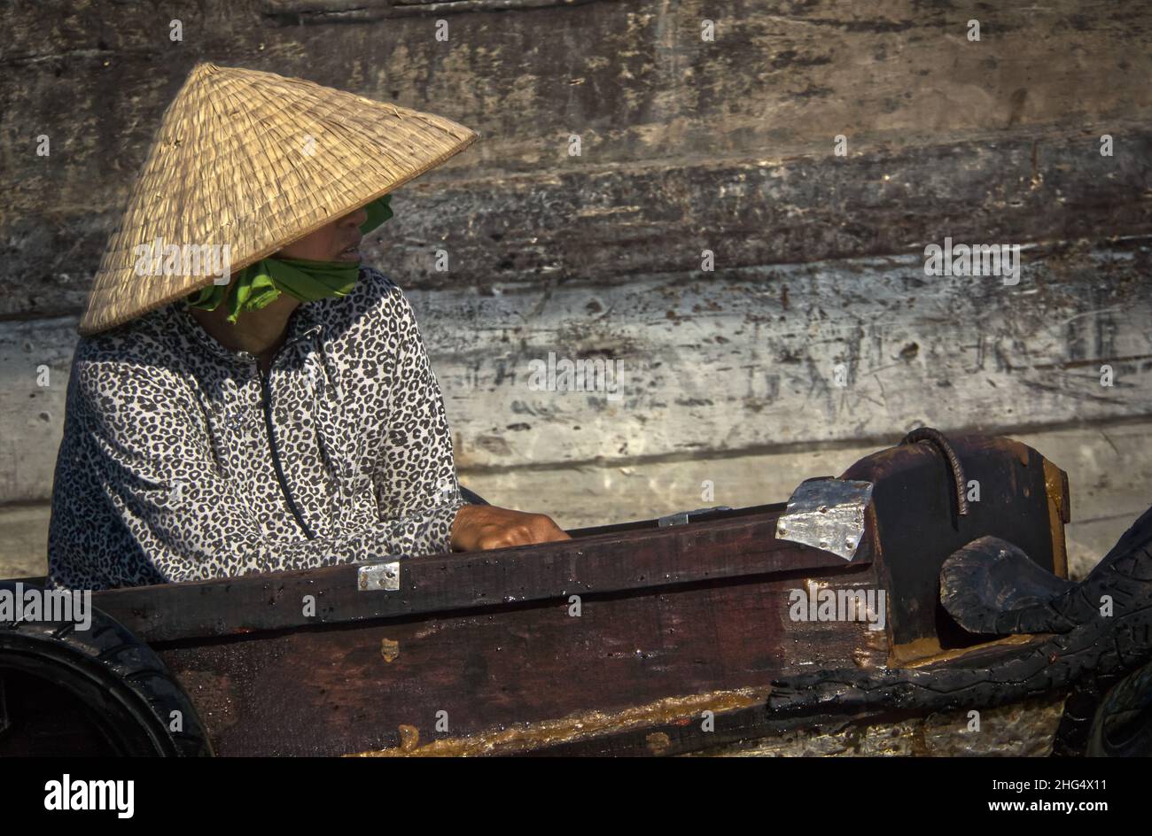 Eine ältere Vietnamesin mit Reishut sitzt in einem kleinen Holzboot auf dem Schwimmenden Markt von Cai Rang in der Nähe von Can Tho Stock Photo