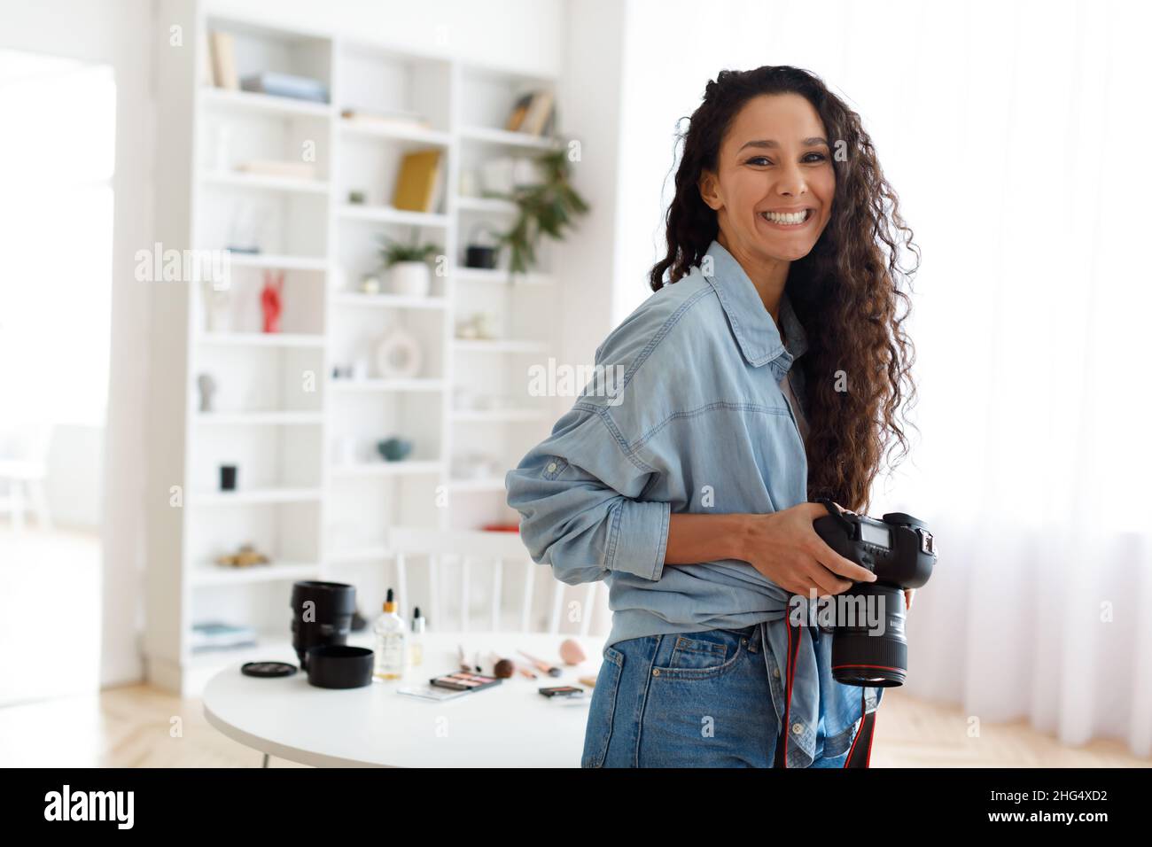 Female Photographer Posing Holding Photocamera Standing In Modern Studio Stock Photo