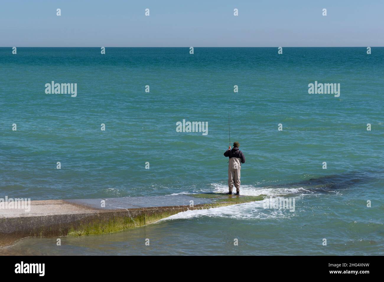 Man wearing waders fishing on the beach Stock Photo