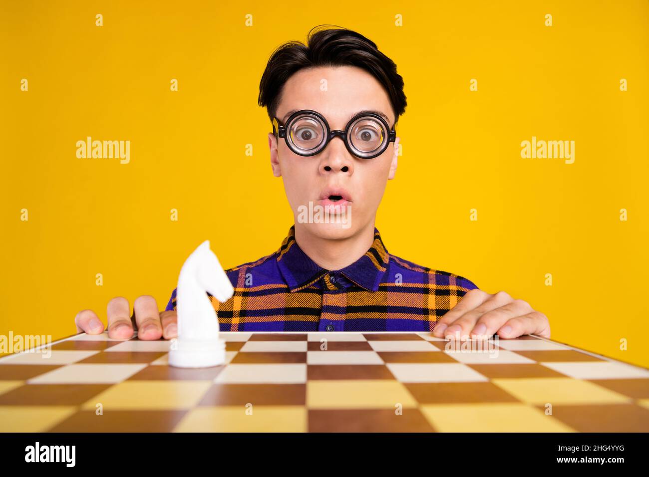 Photo of young impressed guy play chess wear checkered shirt spectacles isolated on yellow color background Stock Photo