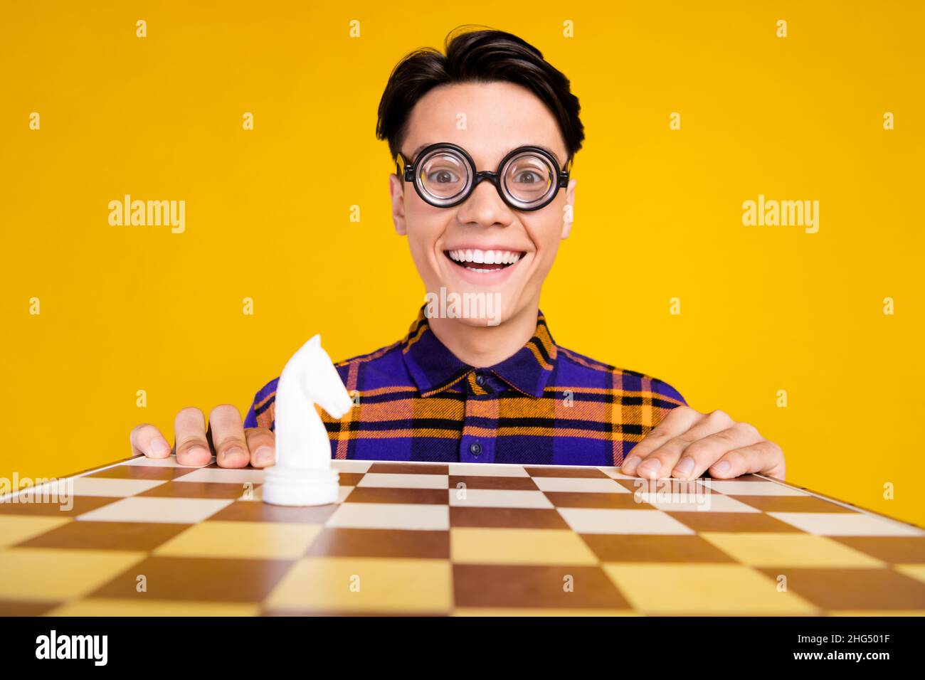 Photo of funny funky teen boy wear plaid outfit spectacles smiling playing chess isolated yellow color background Stock Photo