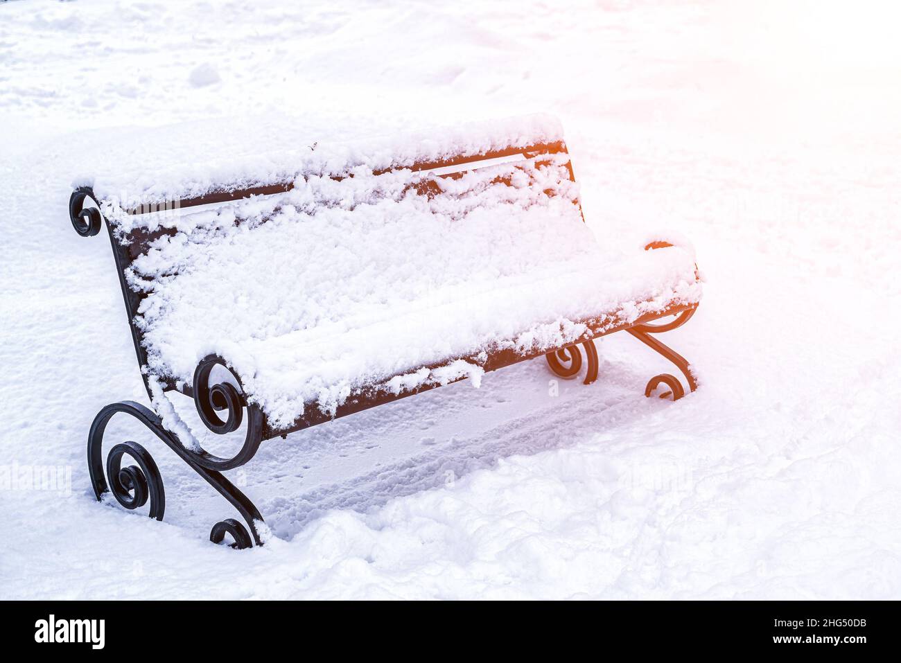 A bench in the park covered with snow and lit by the sun in winter ...