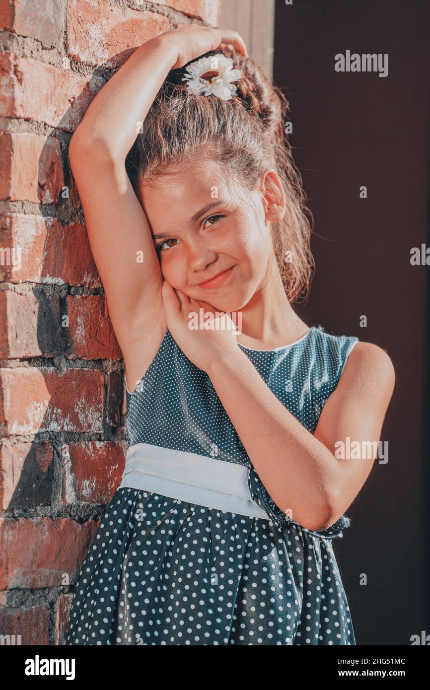 a young brunette girl in a blue polka dot dress stands against the wall ...