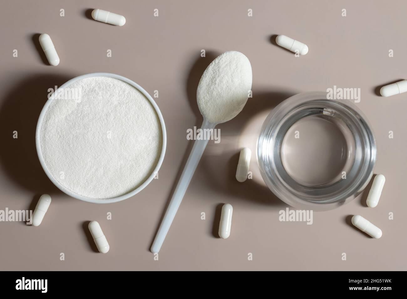 Collagen powder, pills and a glass of water on a beige background close ...