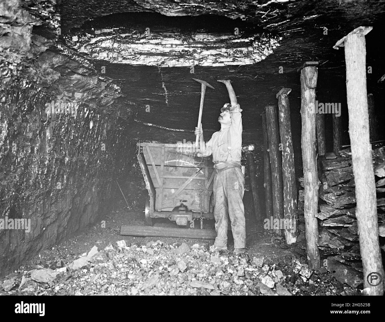 Coal miner using a pick next to a coal wagon in an American coal mine circa 1910 showing the dirty and cramped conditions they worked in Stock Photo
