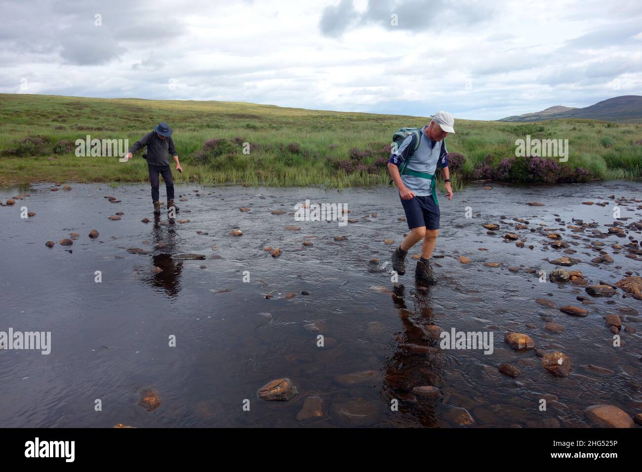 Two Men Walking Through River to the Scottish Mountain Corbett 'Ben Loyal' near Cunside, Tongue, Sutherland, Scottish Highlands, Scotland, UK. Stock Photo