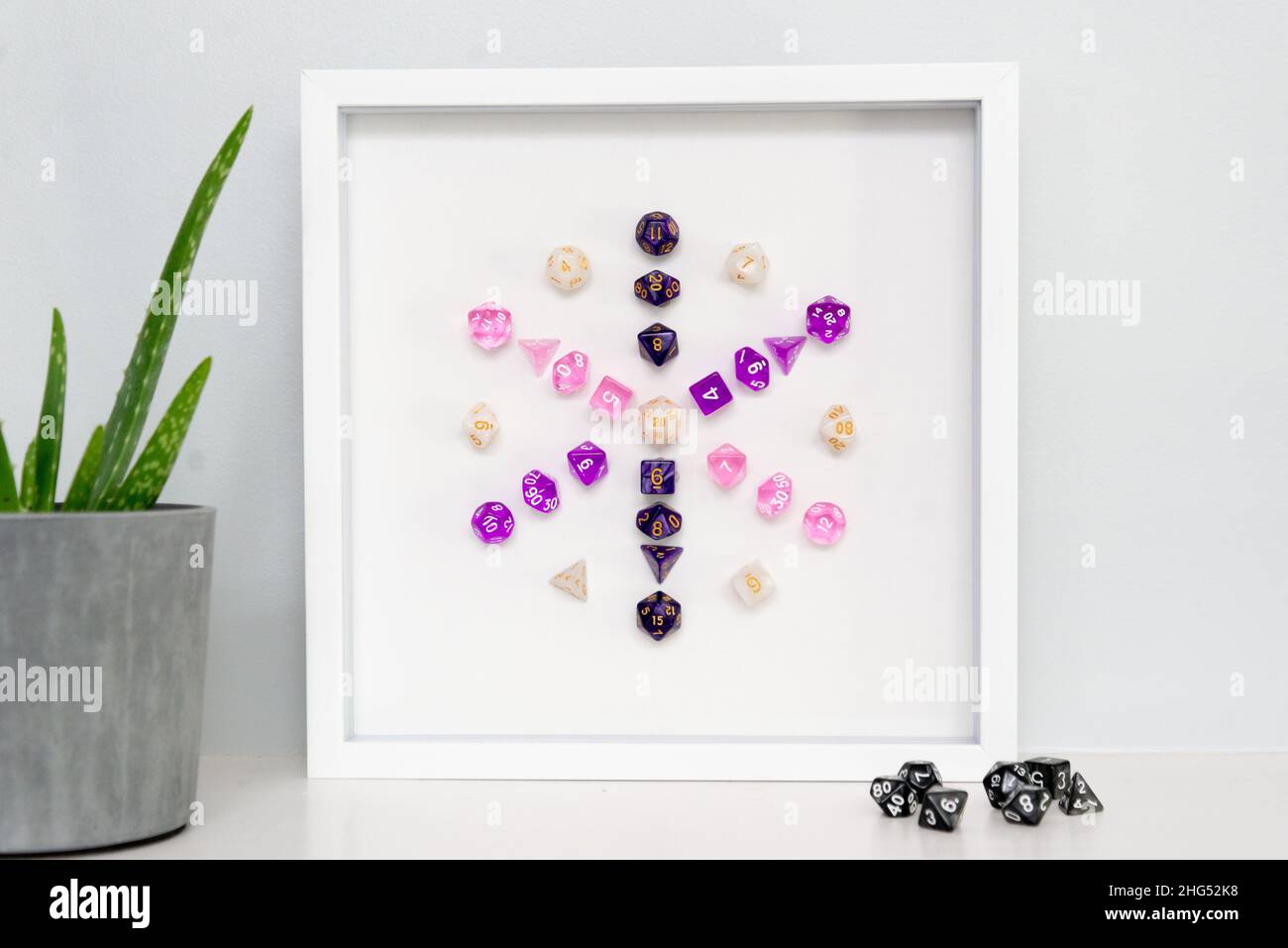 A framed piece of minimalist mixed-media art: a dice mandala created with colorful polyhedral dice used for role playing games like D&D. Stock Photo