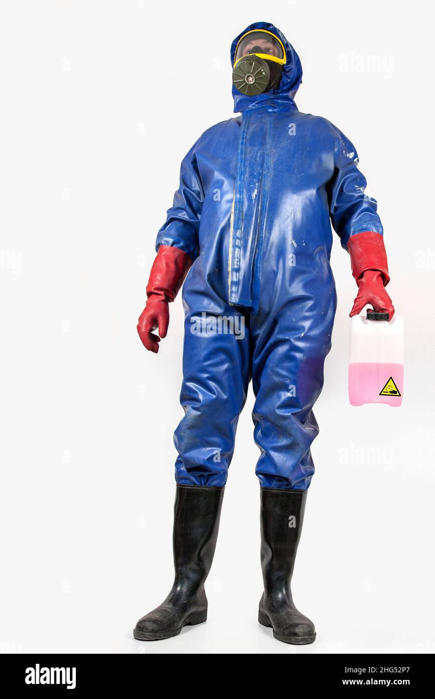 Man in blue rubber blue rubber protective suit, with gas mask, rubber gloves and black rubber boots holds a canister withcleaning liquid in his hand. Stock Photo