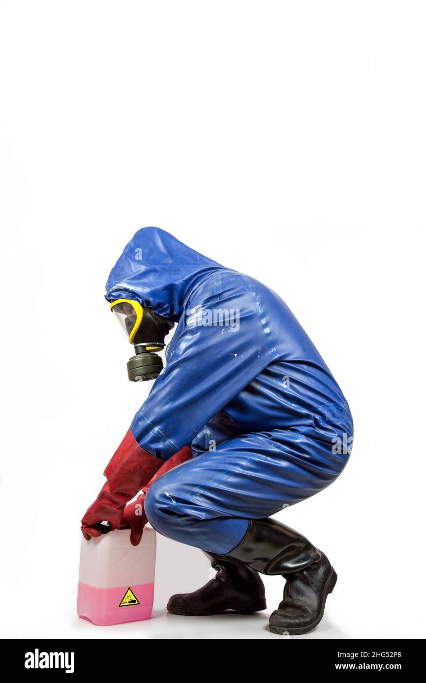 Man in blue rubber blue rubber protective suit, with gas mask, red rubber gloves and black rubber boots opens a canister. Stock Photo