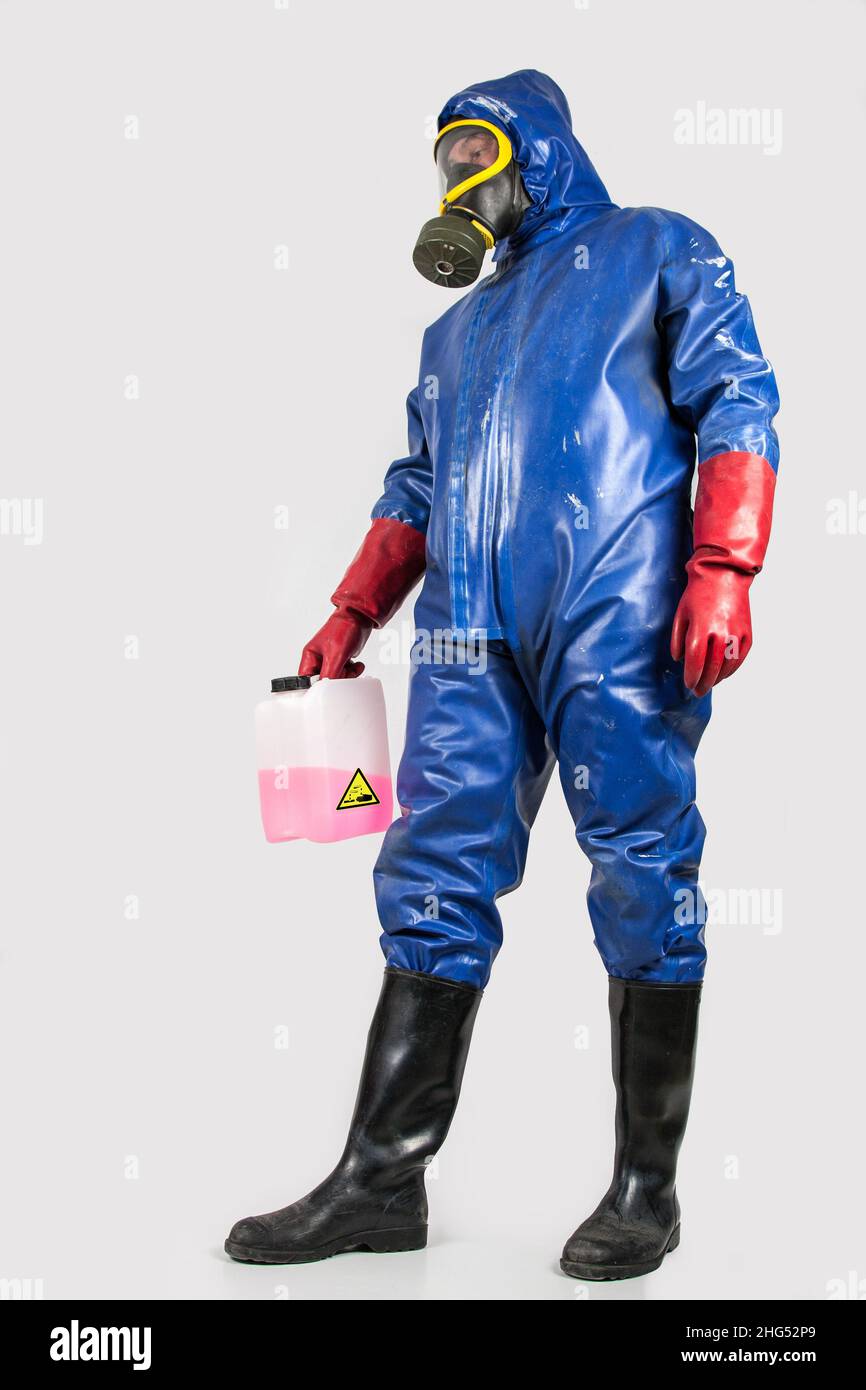 Man in blue rubber protective suit, holds a canister with a red and corrosive cleaning liquid in his hand. Stock Photo