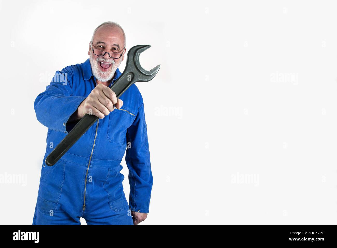 Funny, dynamic senior craftsman with great experience holds a giant open-end wrench in his hand. Stock Photo
