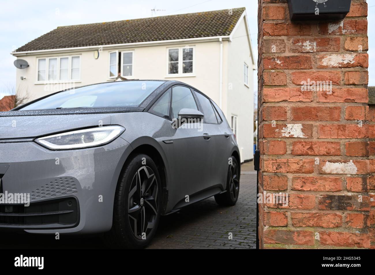A view of an electric grey car leaving a rural property with a cream render passing a brick pillar on a block drivewayV Stock Photo