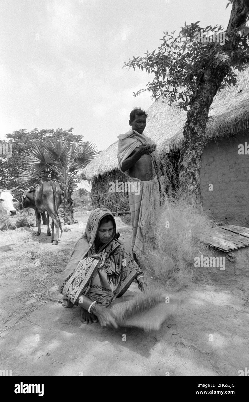 B/W of a poor fisherman mending his nets and his wife winnowing rice at their homestead in rural Odisha (Orissa). Eastern India. Stock Photo