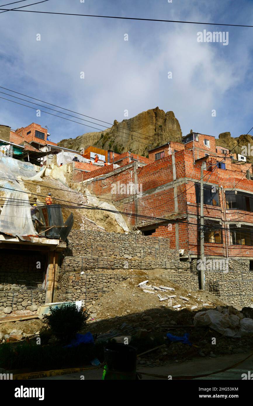 La Paz, Bolivia: Municipal workers stabilising a hillside and damaged houses with cages filled with rocks / gabions at a site in Tembladerani / Cotahuma district. Unauthorised excavation and earth moving by one of the property owners caused part of the hillside to collapse. Many of La Paz's hillside neighbourhoods have been built in unstable areas without proper permits or building controls. Subsidence and erosion causing landslides and houses to collapse are common, especially in the rainy season. In this incident 2 houses had to be demolished and 6 others were badly affected. Stock Photo
