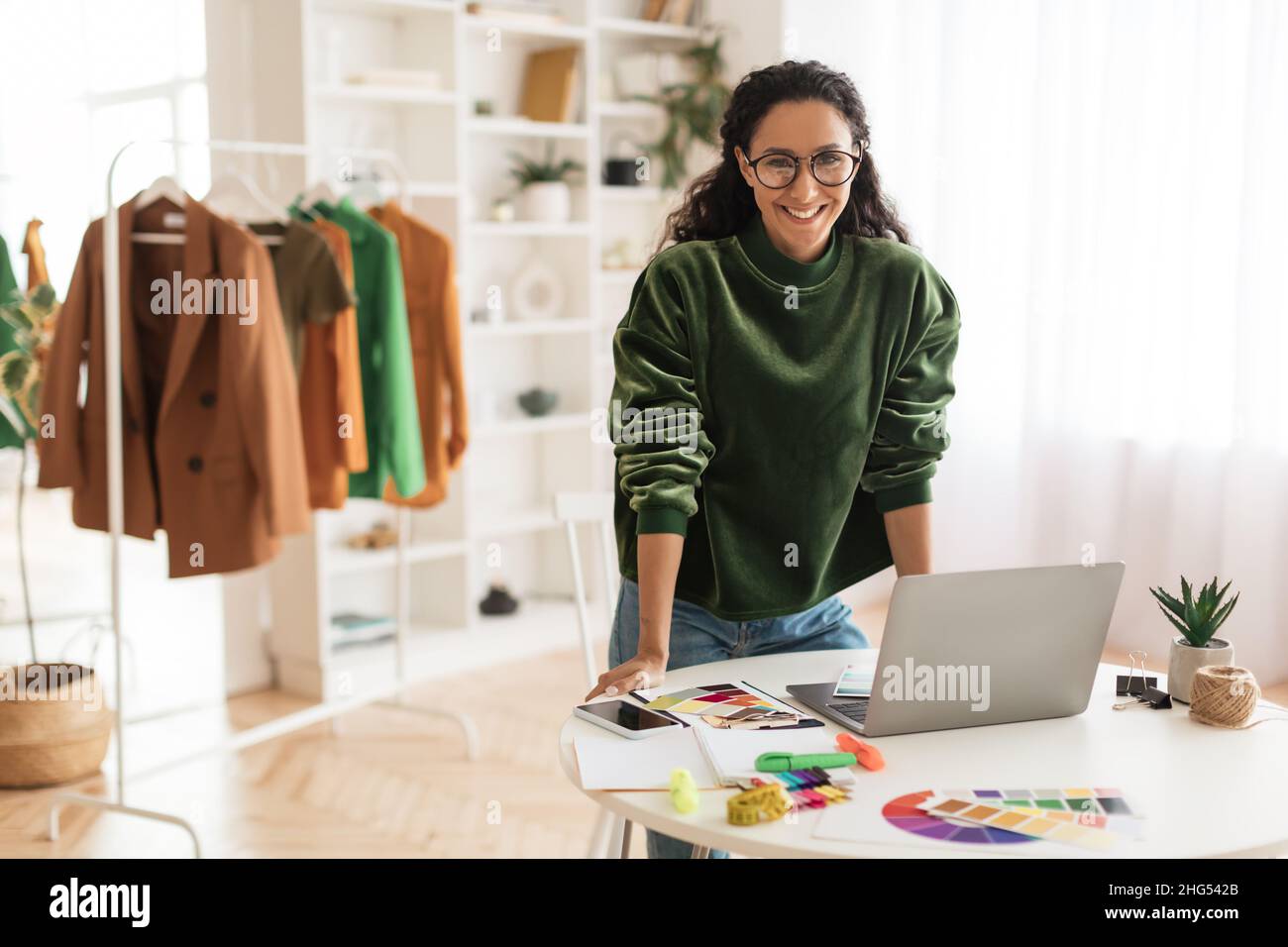 Happy Clothing Designer Lady Using Laptop Smiling Standing In Showroom Stock Photo