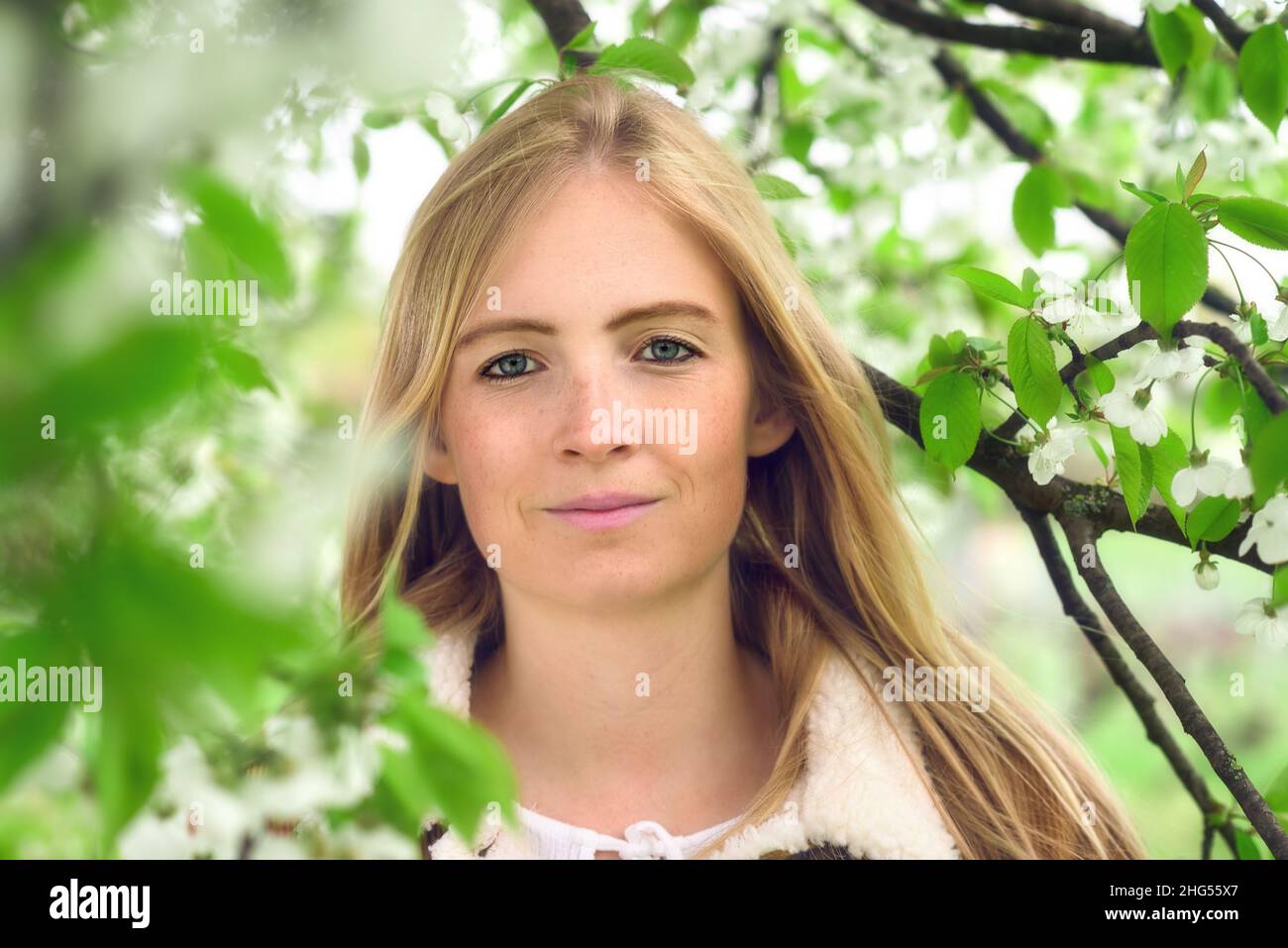 Portrait of a beautiful young woman in nature, with spring blossoms and tender green foliage on tree branches surrounding her face Stock Photo