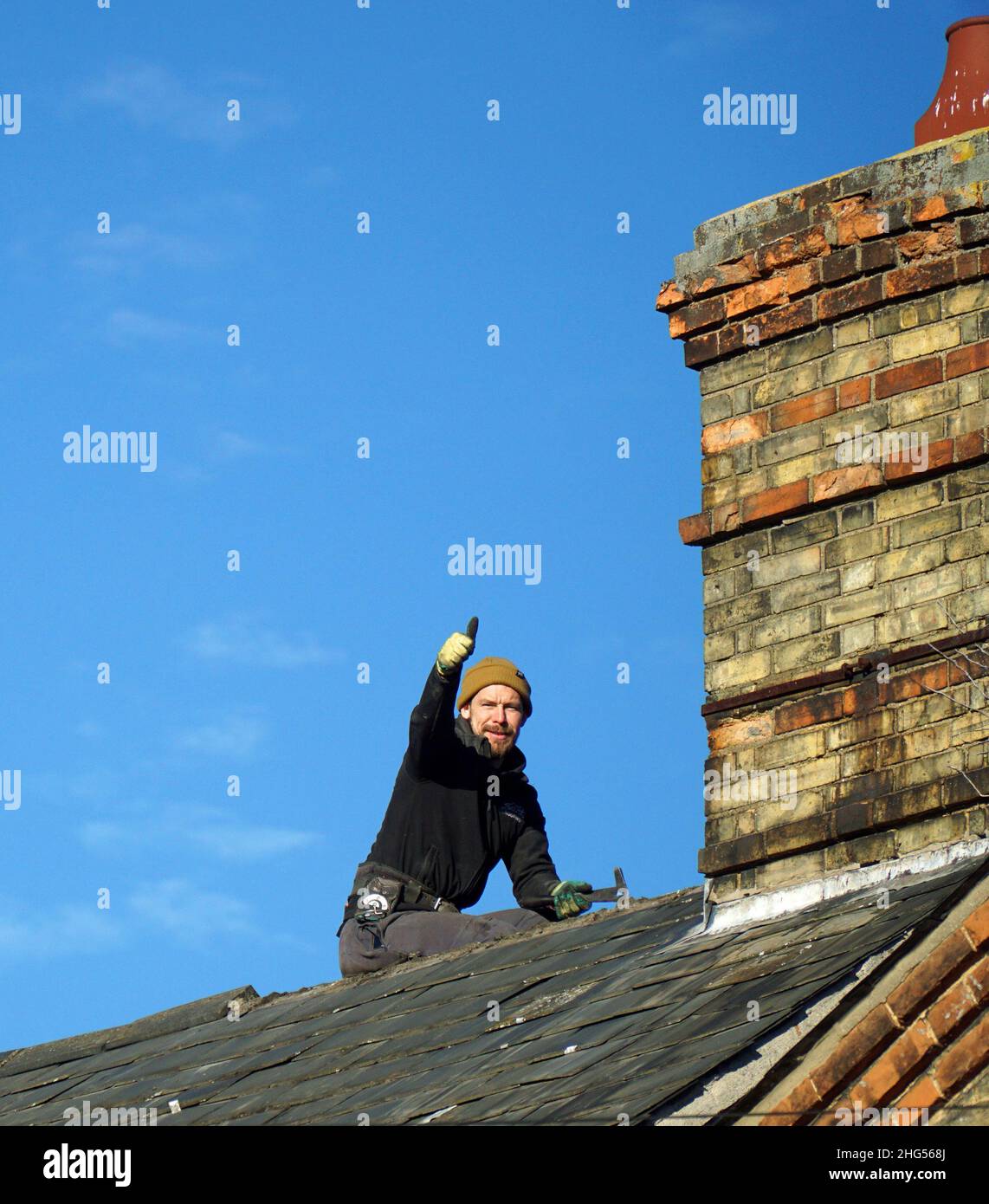 Workman on house roof doing repairs and Victorian Chimney. Stock Photo