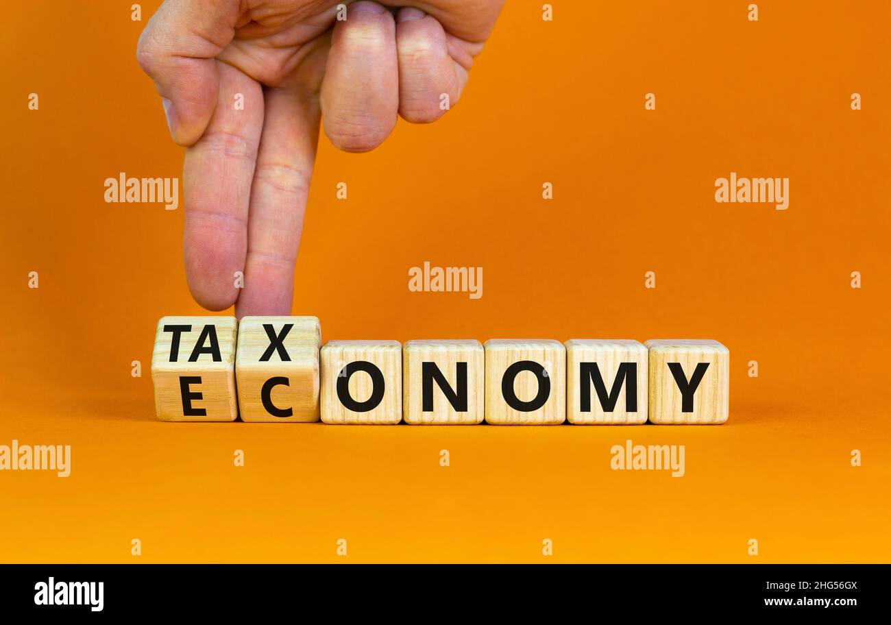Taxonomy or economy symbol. Businessman turns cubes, changes the word economy to taxonomy. Beautiful orange table, orange background, copy space. Busi Stock Photo