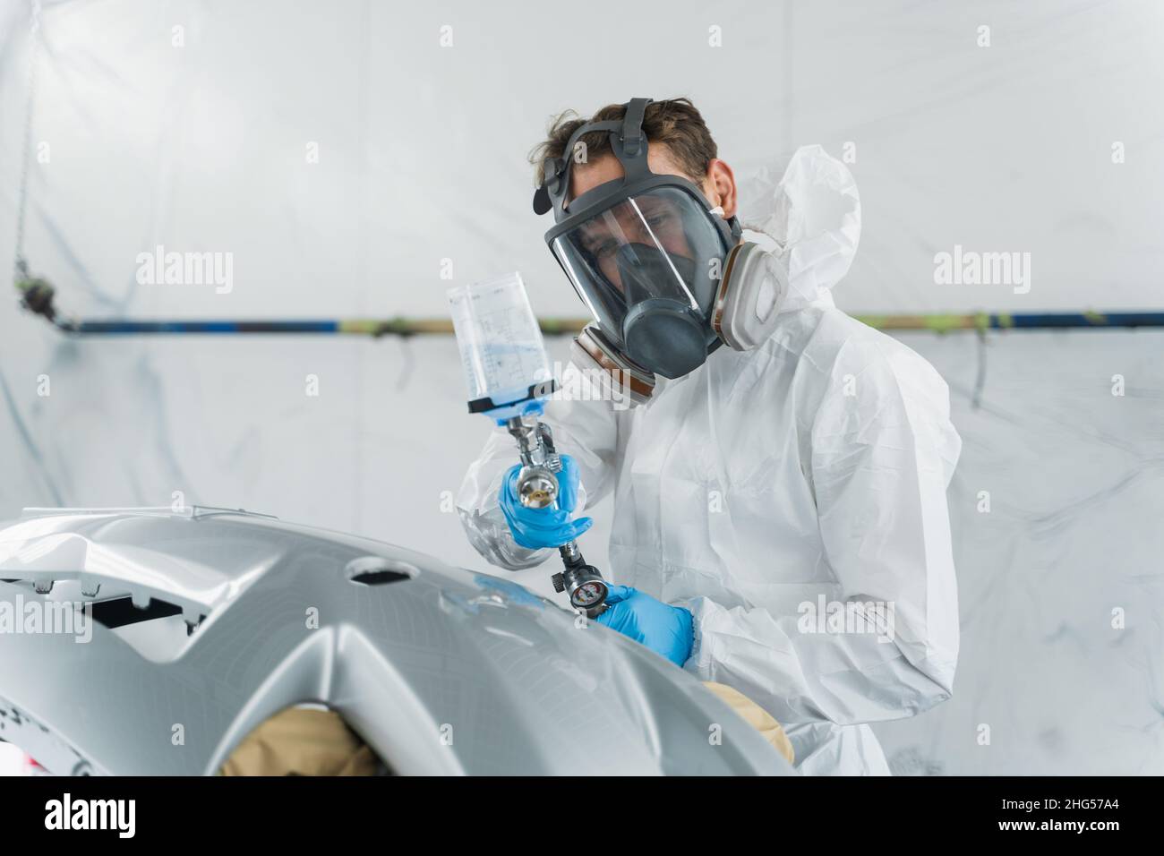 Auto painter varnishing a car body part in a painting booth. Repairman