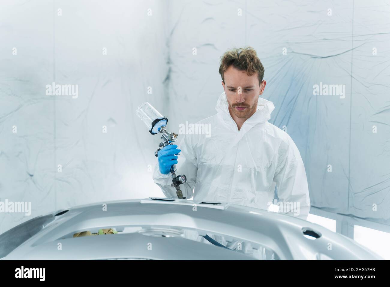 Car service worker with a paint gun in his hand works in a automobile ...