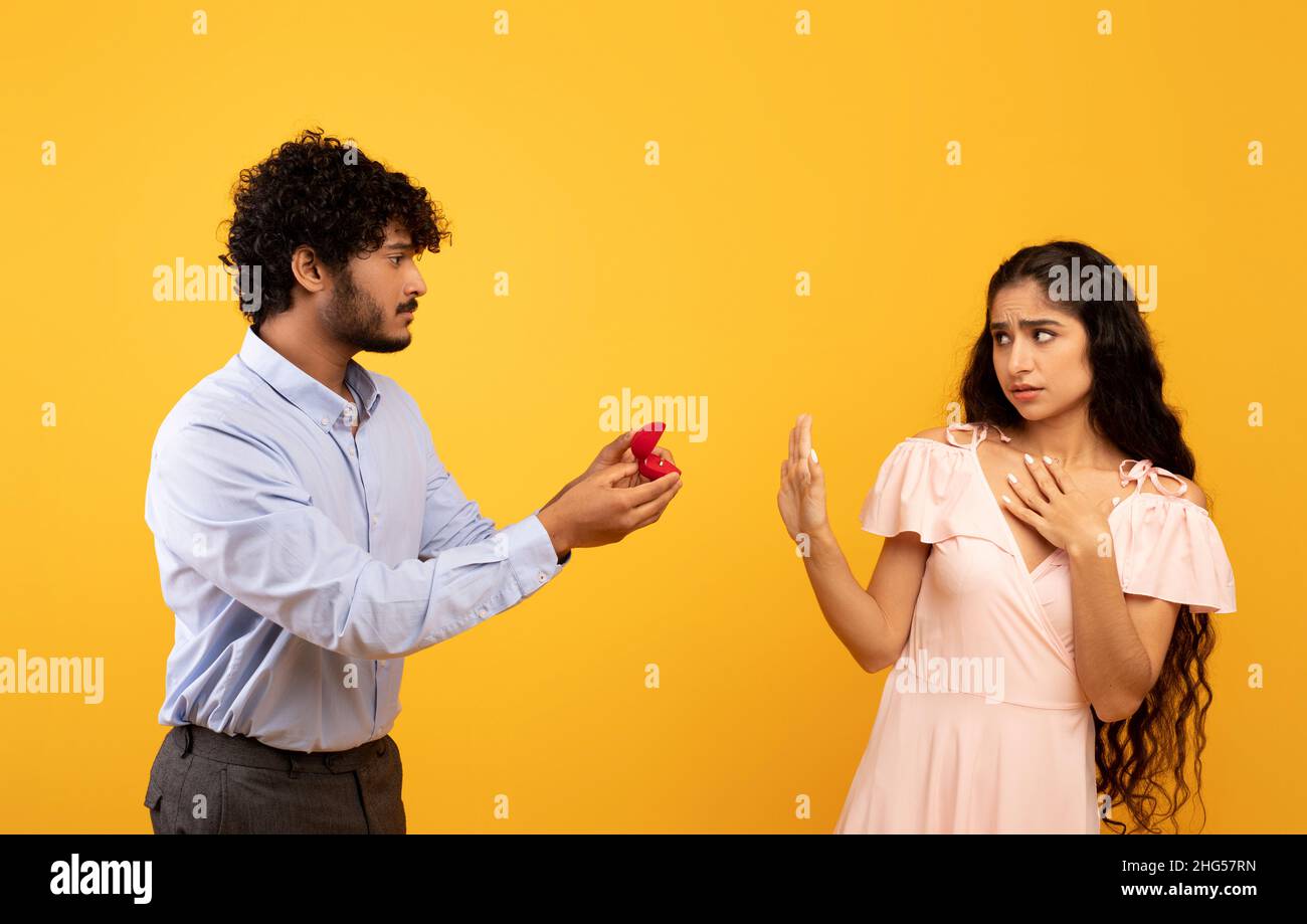 Declining proposal. Indian woman refusing to take engagement ring rejecting boyfriend, standing over yellow background Stock Photo