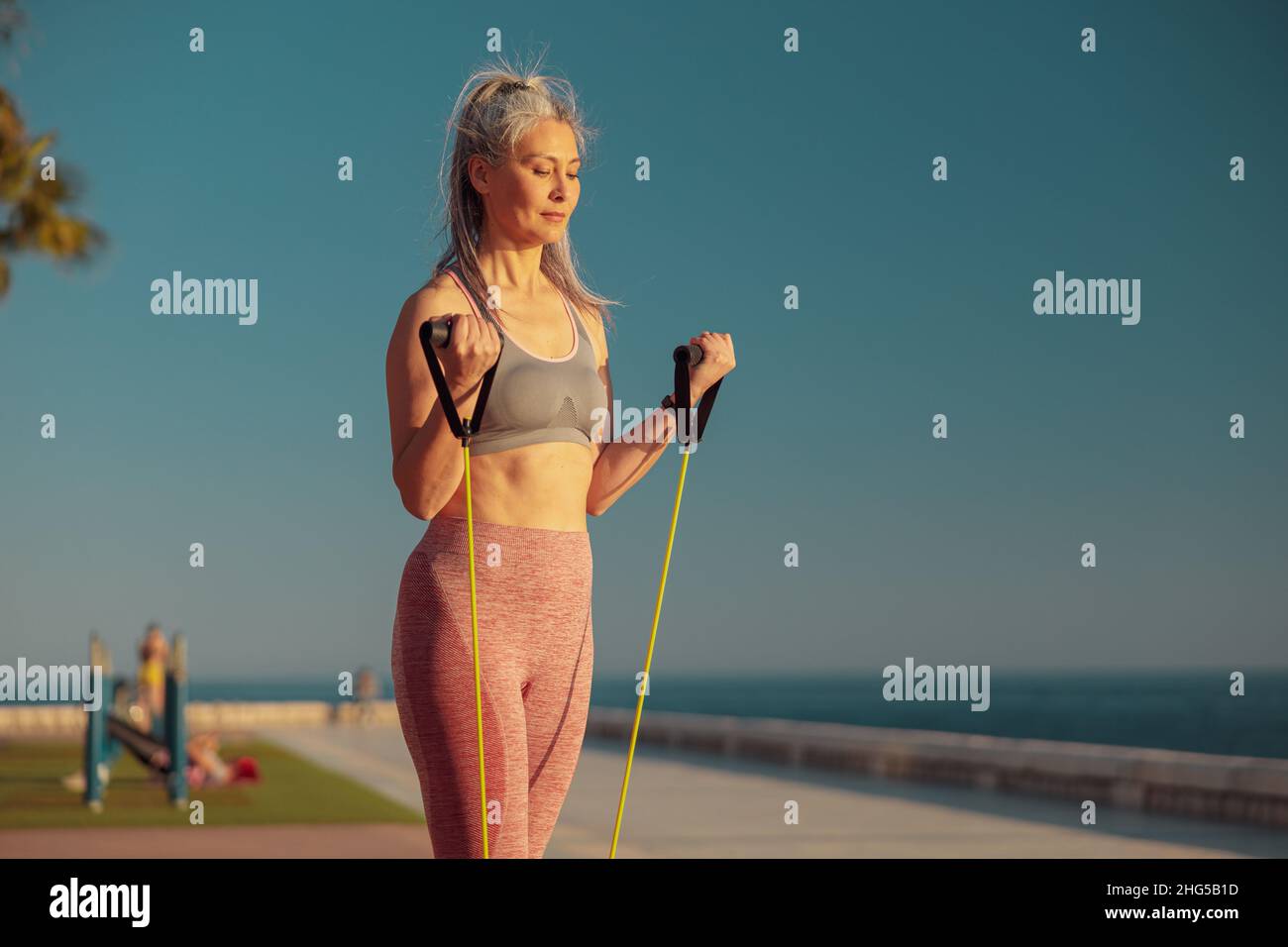 Portrait of woman exercising with fitness resistance bands on the sports site on seashore Stock Photo