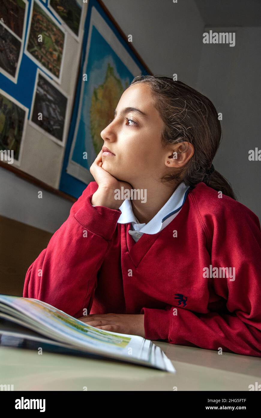 SCHOOL PUPIL GIRL DAYDREAMING PENSIVE CLASS ASIAN HISPANIC GIRL 12-14 years Junior girl student gazes out of school classroom window, dreaming. Stock Photo