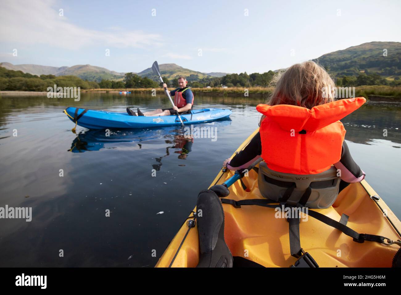 young seven year old girl wearing lifejacket in the front of a two person kayak as man paddles past on windermere in summer lake district, cumbria, en Stock Photo